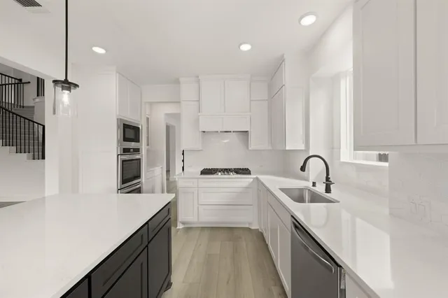 a kitchen with stainless steel appliances sink a stove and white cabinets