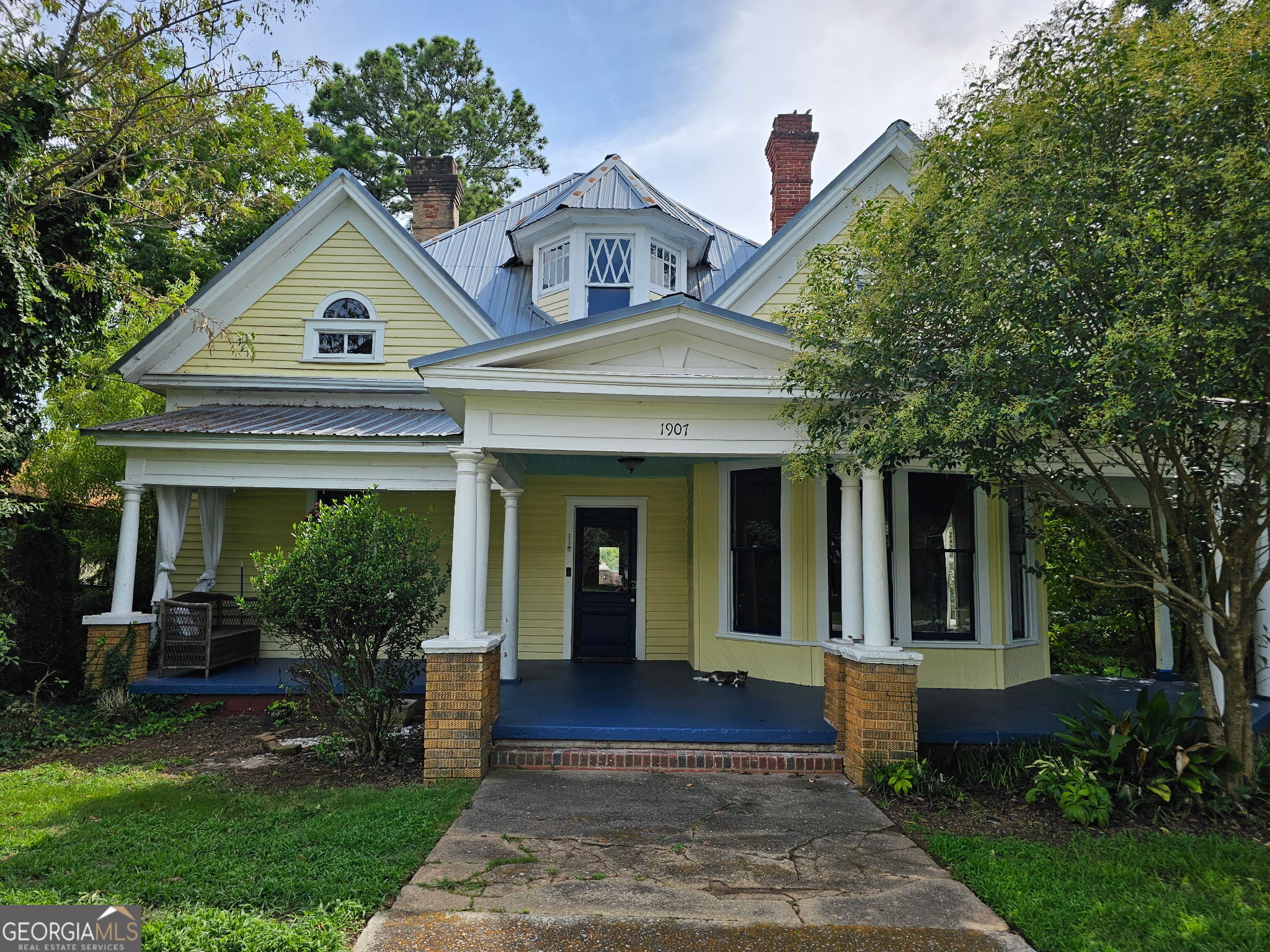 a view of a brick house with a large windows and a yard with plants and large trees