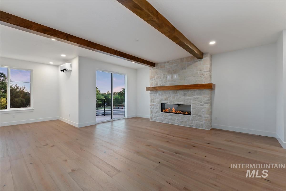 3213 West Moore Street Boise, ID 83702 - Photo 6 of 32 Expansive living space featuring light wood-finish flooring, a stone-clad fireplace with a wood mantel, exposed ceiling beams, recessed lighting, and a sliding glass door to an exterior balcony