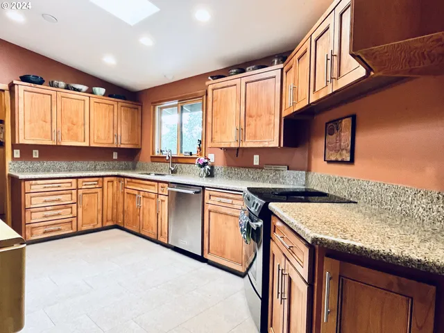 a kitchen with stainless steel appliances granite countertop a sink a stove cabinets counter space and a window