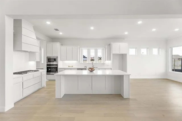 a large white kitchen with stainless steel appliances granite countertop a stove a sink a refrigerator and white cabinets