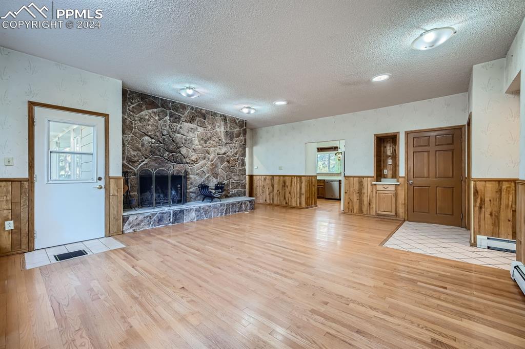 11330 Holmes Road Colorado Springs, CO 80908 - Photo 11 of 40 Unfurnished living room featuring a stone fireplace, a textured ceiling, light hardwood / wood-style flooring, and baseboard heating