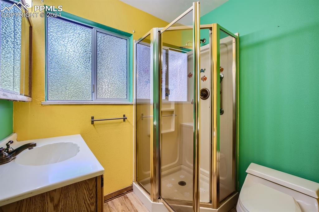 11330 Holmes Road Colorado Springs, CO 80908 - Photo 14 of 40 Bathroom featuring a shower with door, toilet, hardwood / wood-style floors, and vanity