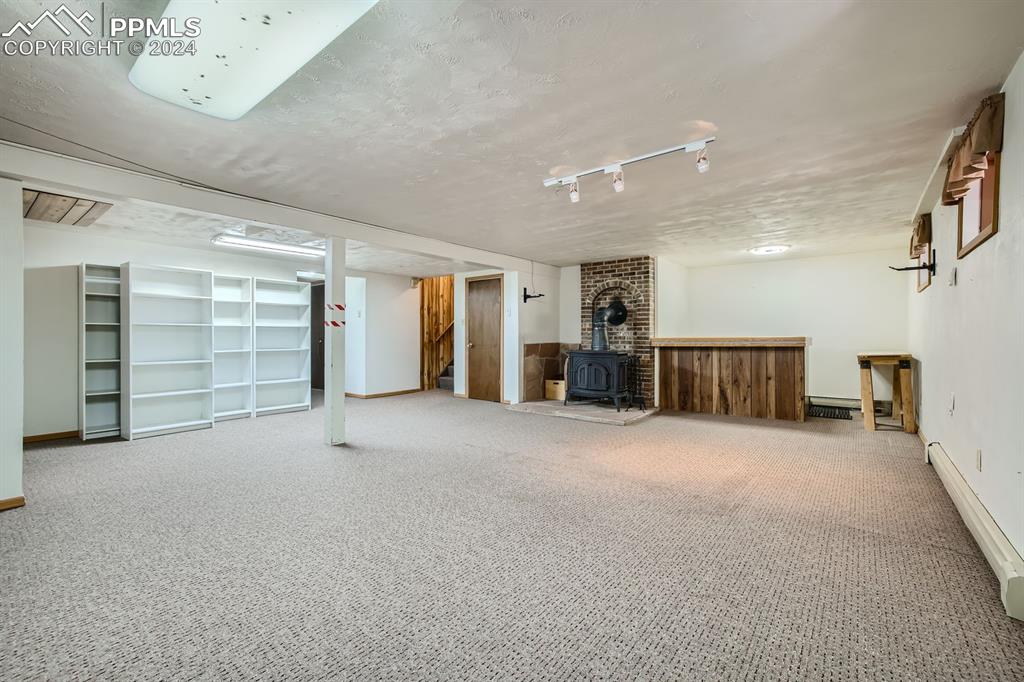 11330 Holmes Road Colorado Springs, CO 80908 - Photo 19 of 40 Basement with a baseboard heating unit, a wood stove, a textured ceiling, and carpet floors
