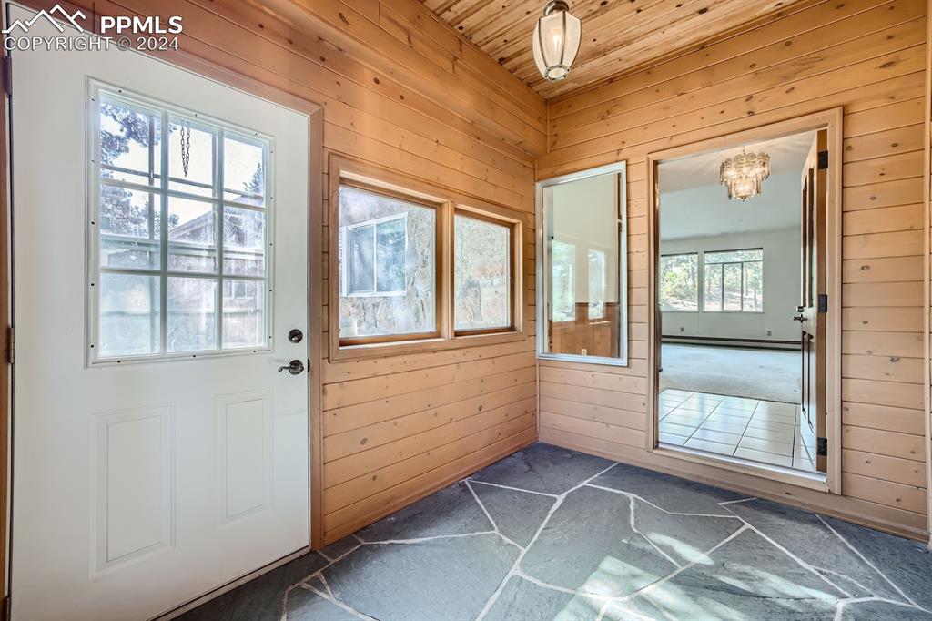 11330 Holmes Road Colorado Springs, CO 80908 - Photo 3 of 40 Front entry with slate floors, with a notable chandelier, wooden walls, and wooden ceiling