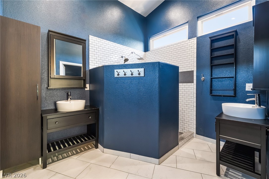261 Timber Hollow Street Henderson, NV 89012 - Photo 33 of 51 A contemporary bathroom with soaring ceilings features dual vanities and a striking central shower with subway tile.