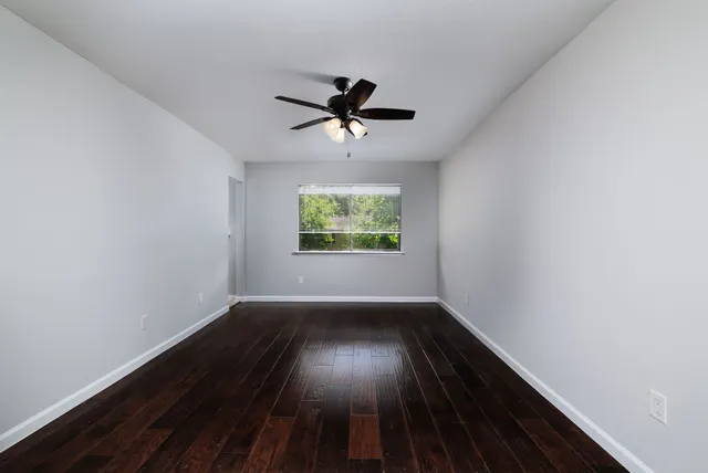 an empty room with wooden floor chandelier fan and windows