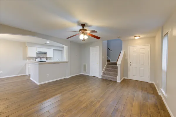 a view of an empty room with wooden floor and a kitchen