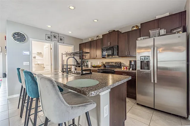 a kitchen with stainless steel appliances granite countertop a refrigerator a sink a stove a dining table and chairs