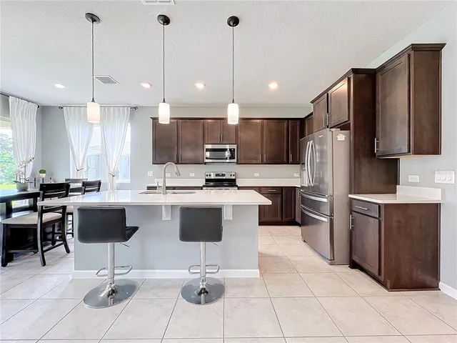 a kitchen with stainless steel appliances kitchen island granite countertop a refrigerator a stove a sink a kitchen island with chairs and white cabinets