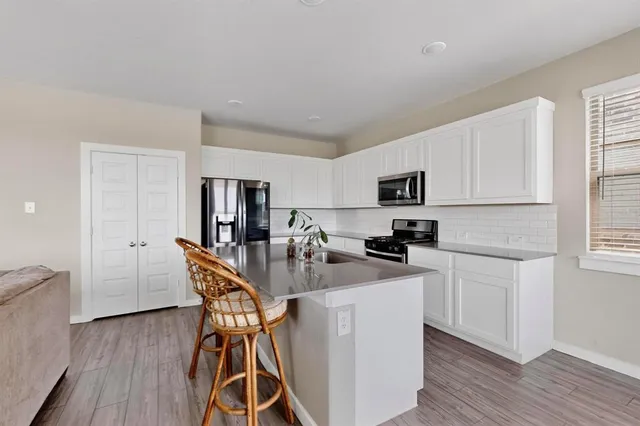 a kitchen with stainless steel appliances kitchen island granite countertop a refrigerator a stove a sink a dining table and chairs with wooden floor