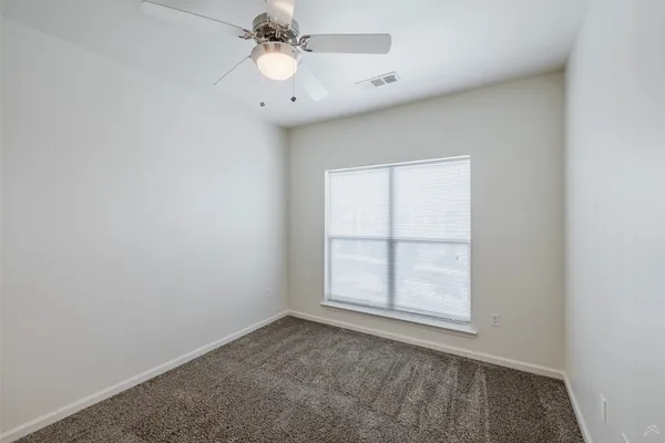 an empty room with chandelier fan and windows