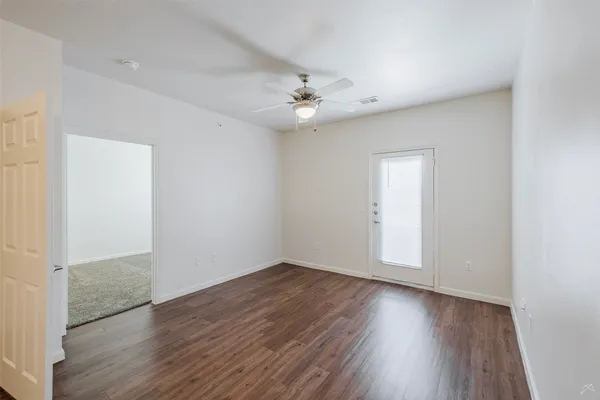 an empty room with wooden floor ceiling fan and windows