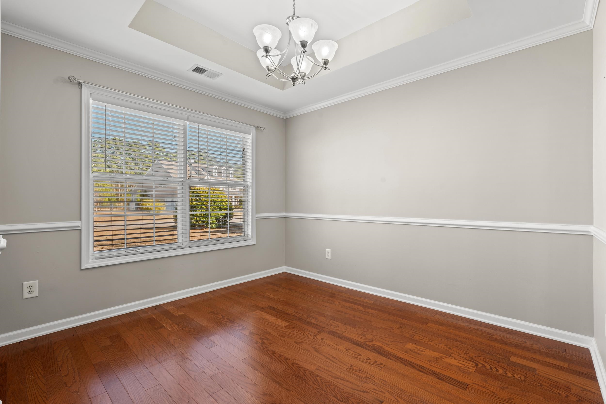 2487 Windmill Way Myrtle Beach, SC 29579 - Photo 15 of 40 Empty room with a raised ceiling, a chandelier, ornamental molding, and dark wood-style floors