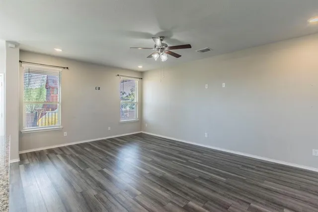 an empty room with wooden floor fan and windows
