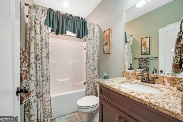 a bathroom with a granite countertop sink a mirror a toilet and shower