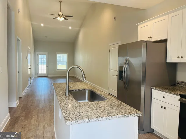 a kitchen with stainless steel appliances granite countertop a refrigerator a sink a stove and white cabinets with wooden floor