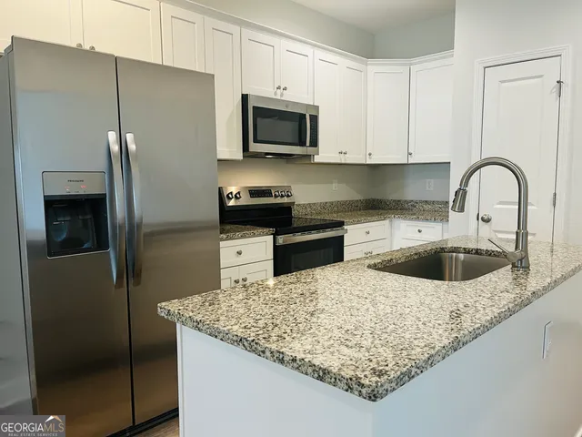 a kitchen with stainless steel appliances granite countertop a refrigerator a stove a sink and a white cabinets