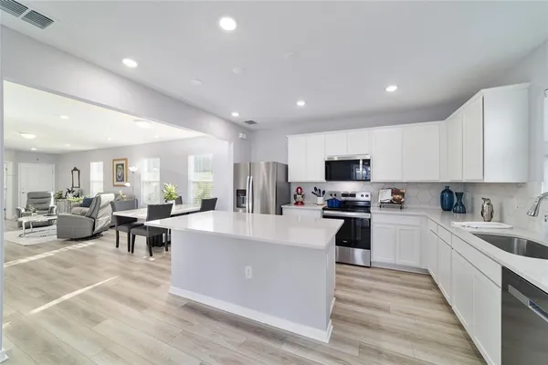 a large white kitchen with kitchen island a sink a counter space and stainless steel appliances