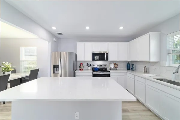 a kitchen with stainless steel appliances a sink a stove a refrigerator with white cabinets