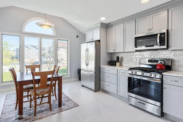 a kitchen with stainless steel appliances granite countertop a stove a refrigerator a microwave a dining table and chairs