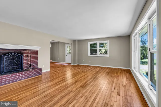 a view of an empty room with wooden floor fireplace and a window