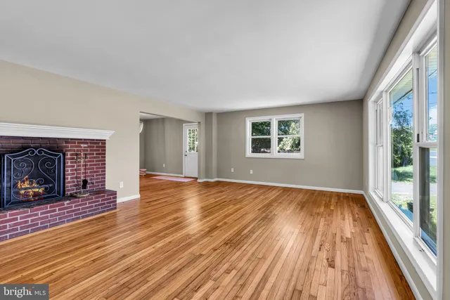 a view of an empty room with wooden floor fireplace and a window