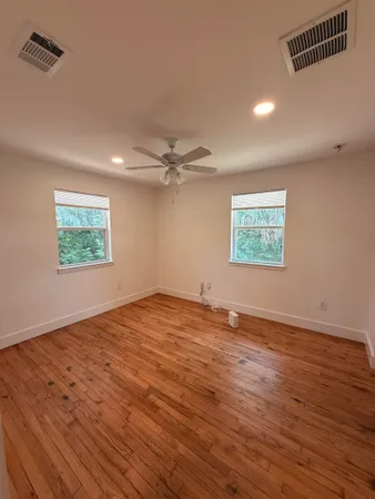 an empty room with wooden floor ceiling fan and windows