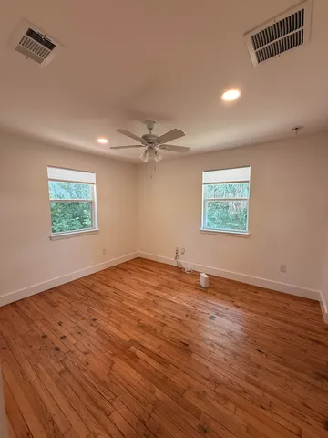 an empty room with wooden floor ceiling fan and windows