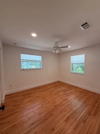 an empty room with wooden floor ceiling fan and windows