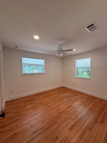 an empty room with wooden floor ceiling fan and windows