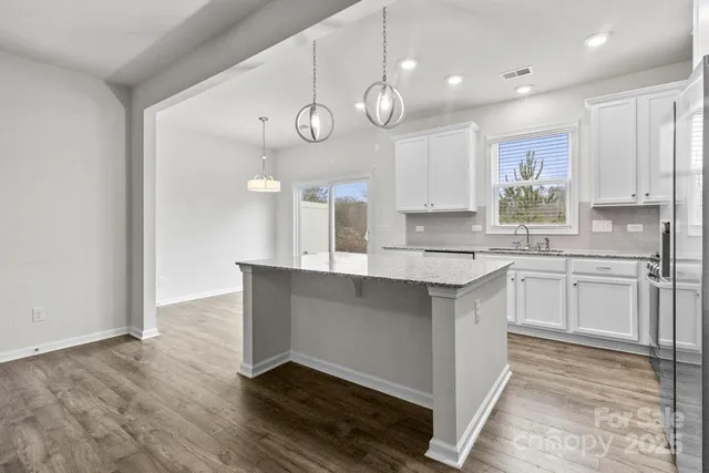 a kitchen with granite countertop a stove a sink and white cabinets with wooden floor