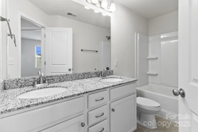 a bathroom with a granite countertop double vanity sink toilet mirror and bathtub