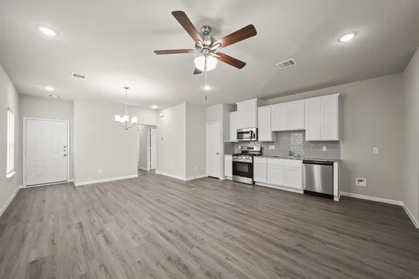 a view of an empty room and kitchen with wooden floor