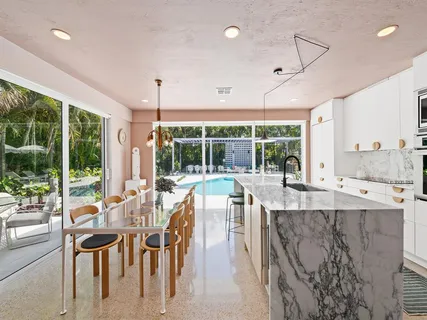 a dining hall with stainless steel appliances granite countertop furniture a large window and a chandelier