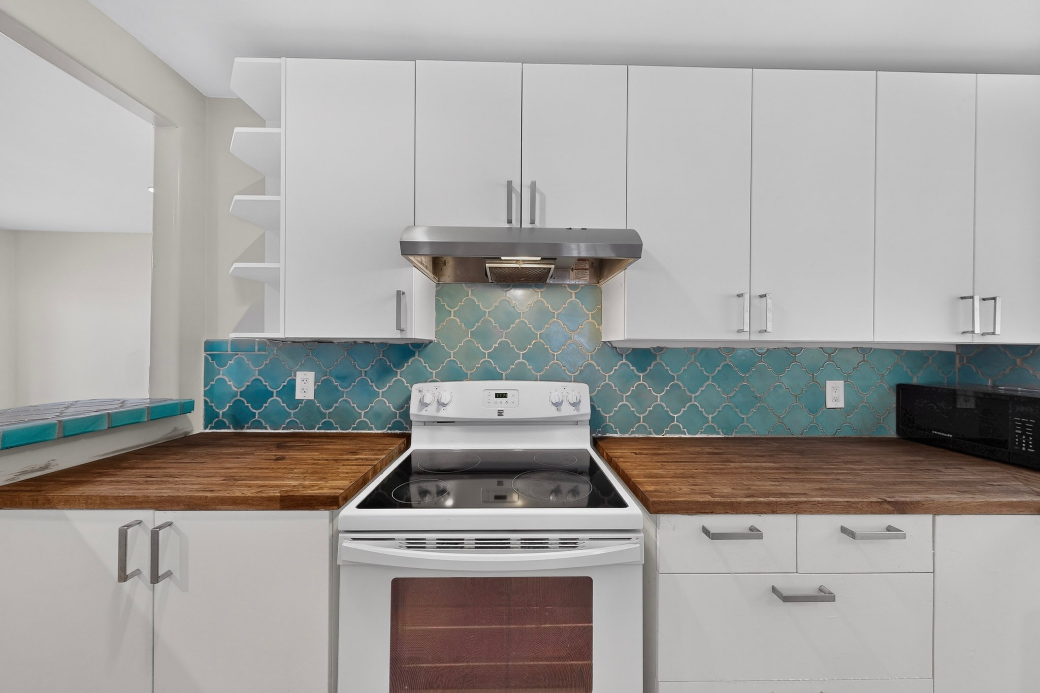 4711 Alf Avenue Austin, TX 78721 - Photo 14 of 34 A well-equipped kitchen features a cooktop and pristine white cabinetry against a vibrant tiled backsplash.