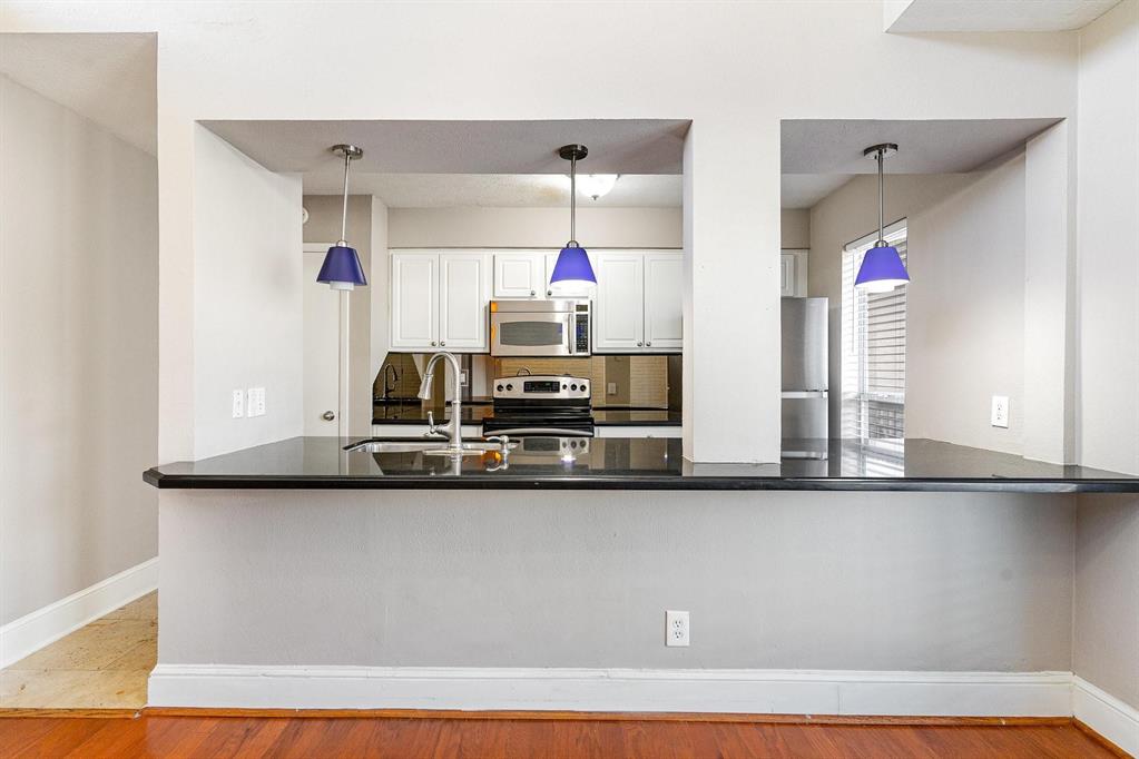 5934 Sandhurst Lane, Unit 207 Dallas, TX 75206 - Photo 4 of 31 Kitchen featuring white cabinetry, a peninsula, stainless steel appliances, decorative light fixtures, and dark stone counters