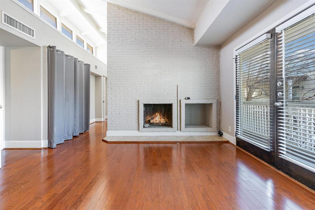 5934 Sandhurst Lane, Unit 207 Dallas, TX 75206 - Photo 6 of 31 Unfurnished living room with a fireplace, hardwood / wood-style flooring, brick wall, and high vaulted ceiling