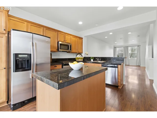 a kitchen with stainless steel appliances granite countertop a refrigerator a stove and a wooden floor