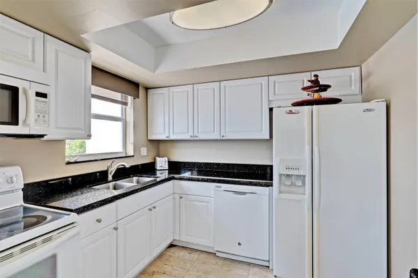 a kitchen with granite countertop white cabinets stainless steel appliances a sink and a window