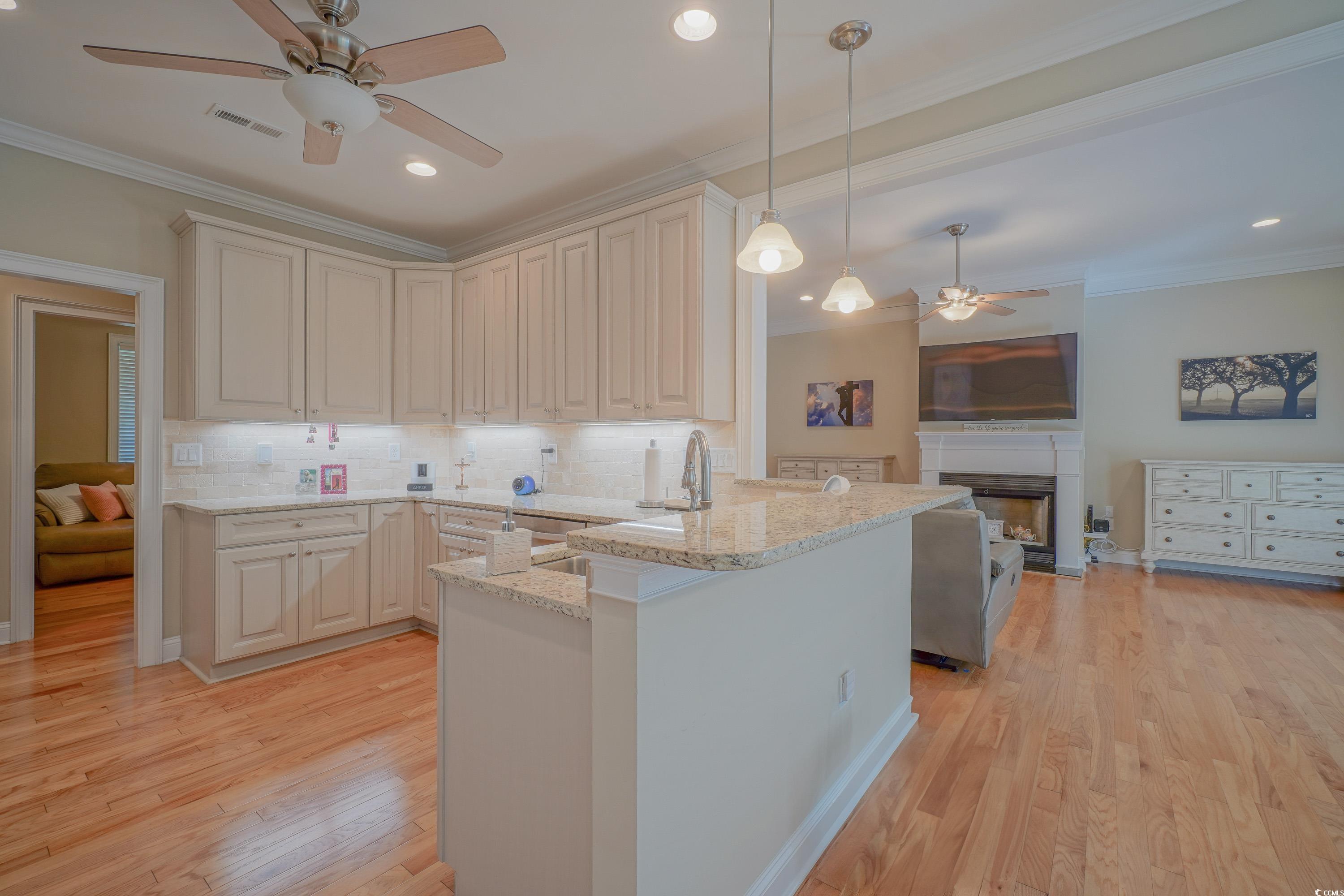 625 Whispering Pines Court Murrells Inlet, SC 29576 - Photo 8 of 36 Kitchen with ceiling fan, light stone counters, a fireplace, a peninsula, and tasteful backsplash