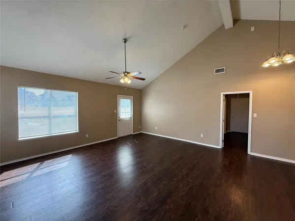 an empty room with wooden floor chandelier and windows