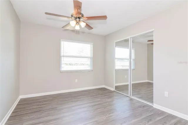 an empty room with wooden floor fan and windows