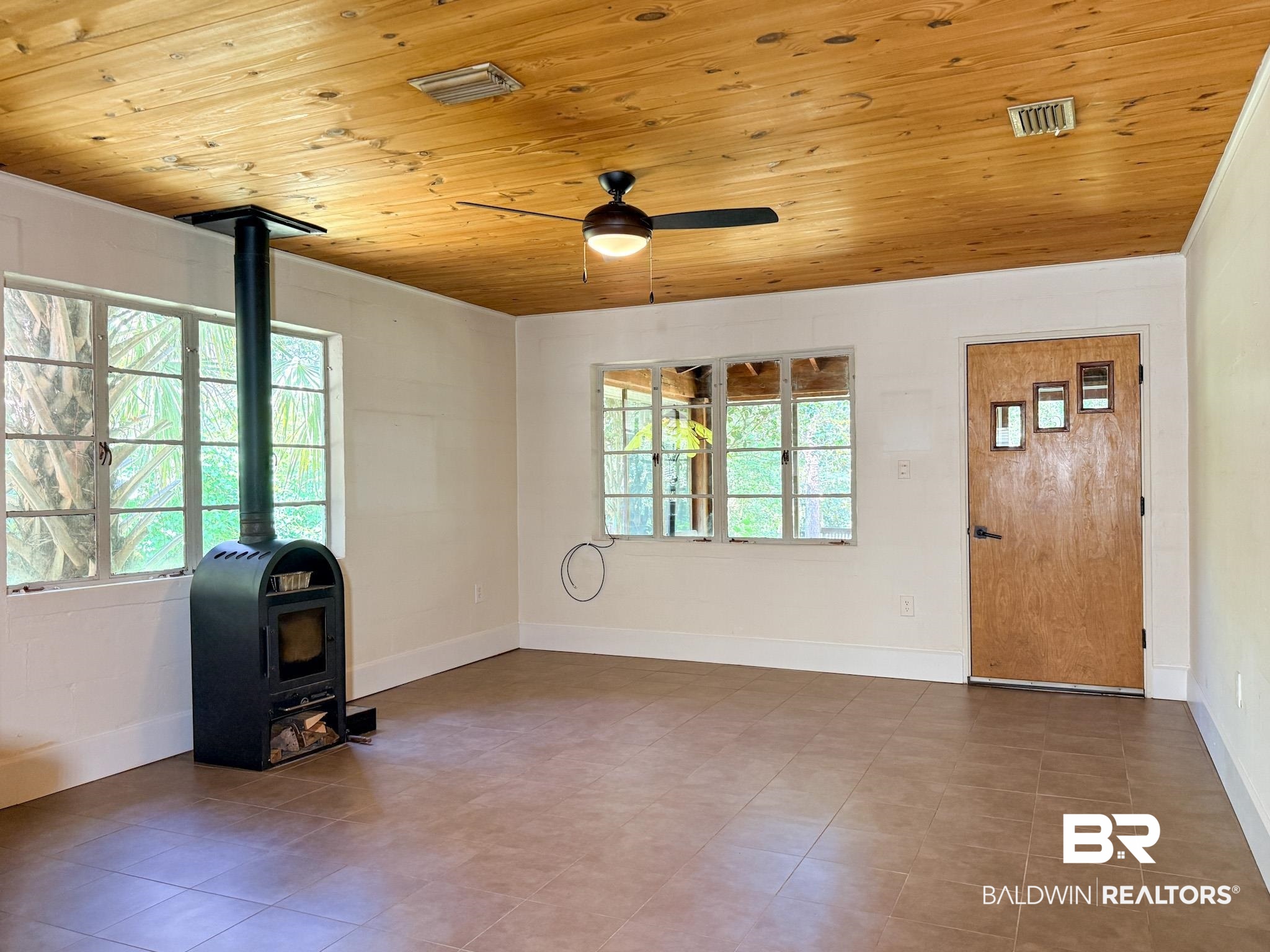 18711 Keller Road Foley, AL 36535 - Photo 3 of 38 Expansive room featuring a wood-panel ceiling, dark tile flooring, and a freestanding black wood-burning stove