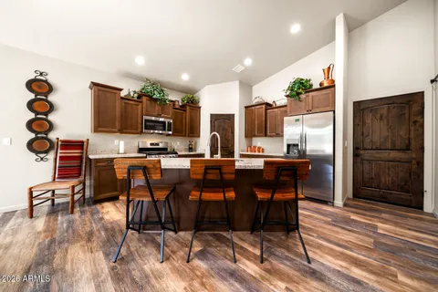 a kitchen with stainless steel appliances kitchen island granite countertop a refrigerator a stove a sink a dining table and chairs with wooden floor