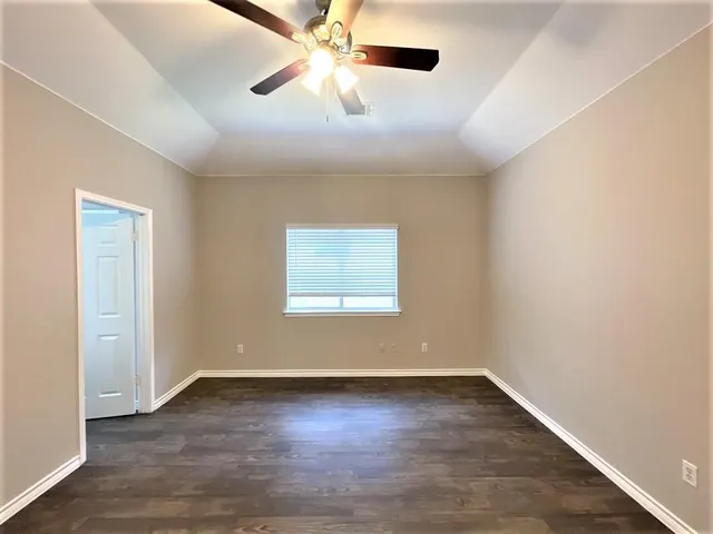 an empty room with wooden floor fan and windows