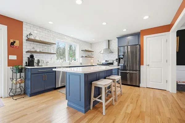 a kitchen with stainless steel appliances kitchen island granite countertop a refrigerator a stove a sink a dining table and chairs with wooden floor