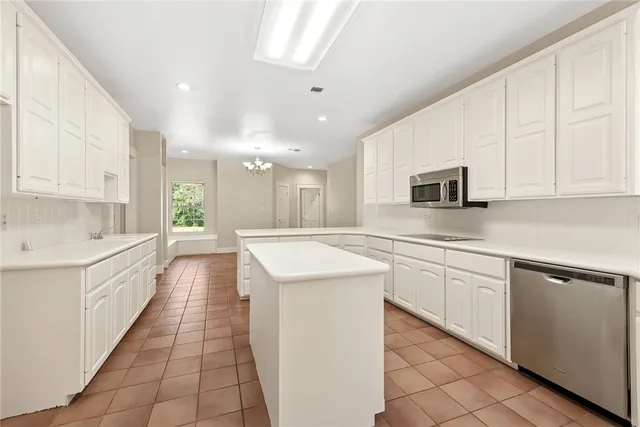 a large kitchen with stainless steel appliances granite countertop a sink and white cabinets