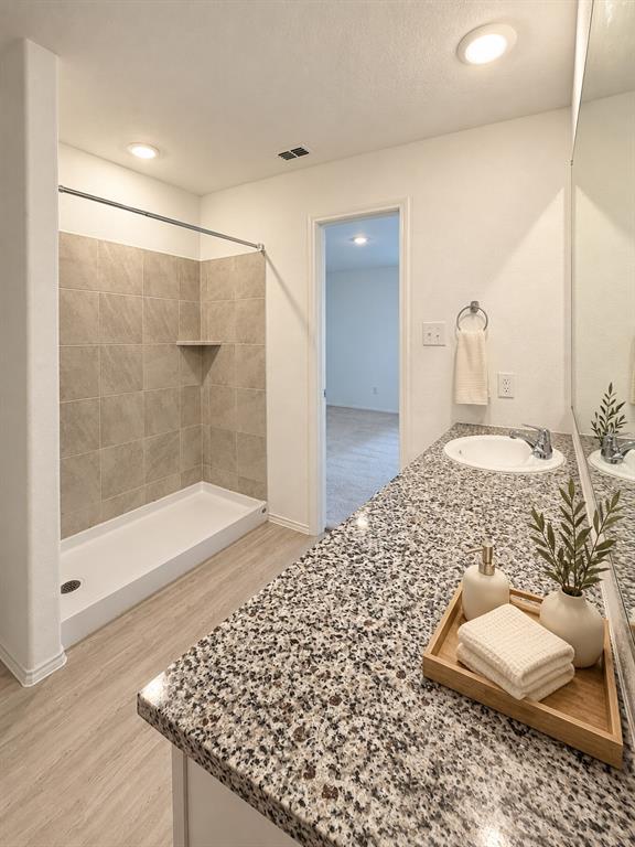 11726 Bone Spg Drive Rhome, TX 76078 - Photo 15 of 29 En-suite primary bath featuring a granite countertop vanity, tiled tub and shower surround, recessed lighting, and luxury vinyl plank flooring.