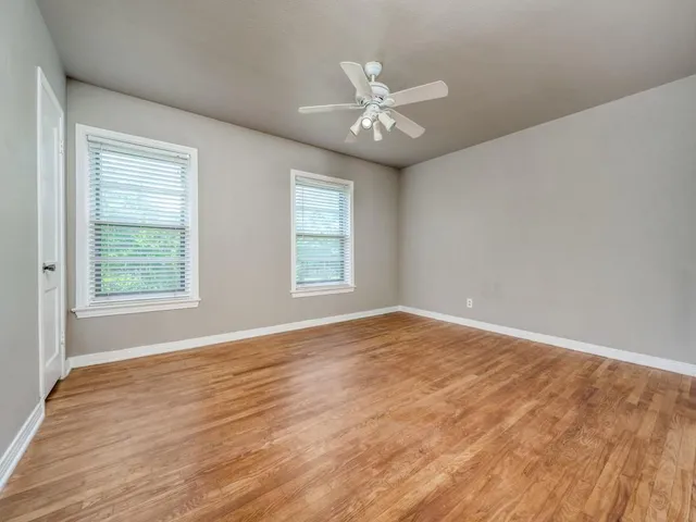 an empty room with wooden floor fan and windows